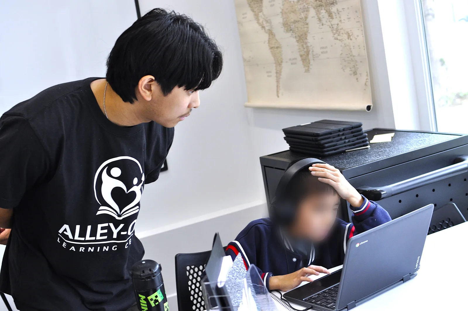 An Alley-Oop Learning Center tutor supporting a young student working on a laptop in the Beacon Hill classroom
